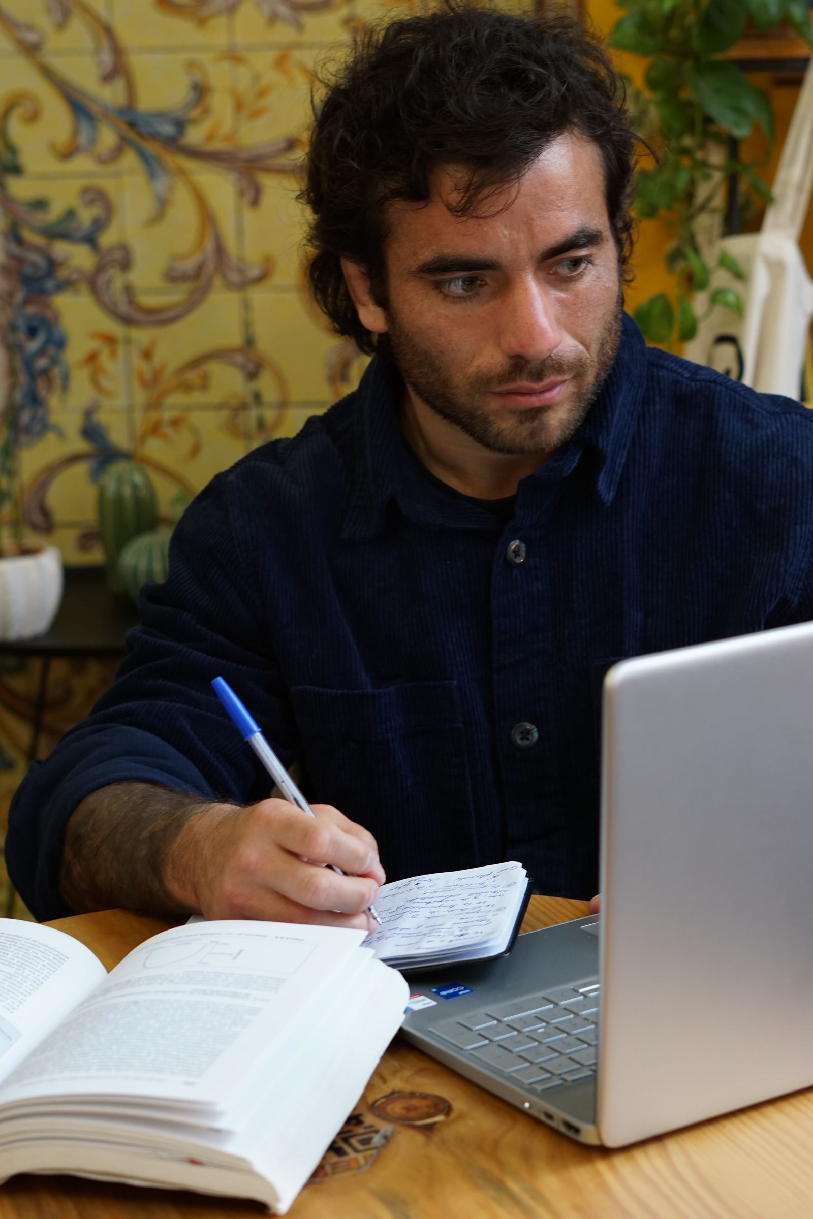 Tomás anotando en su cuaderno junto al portátil